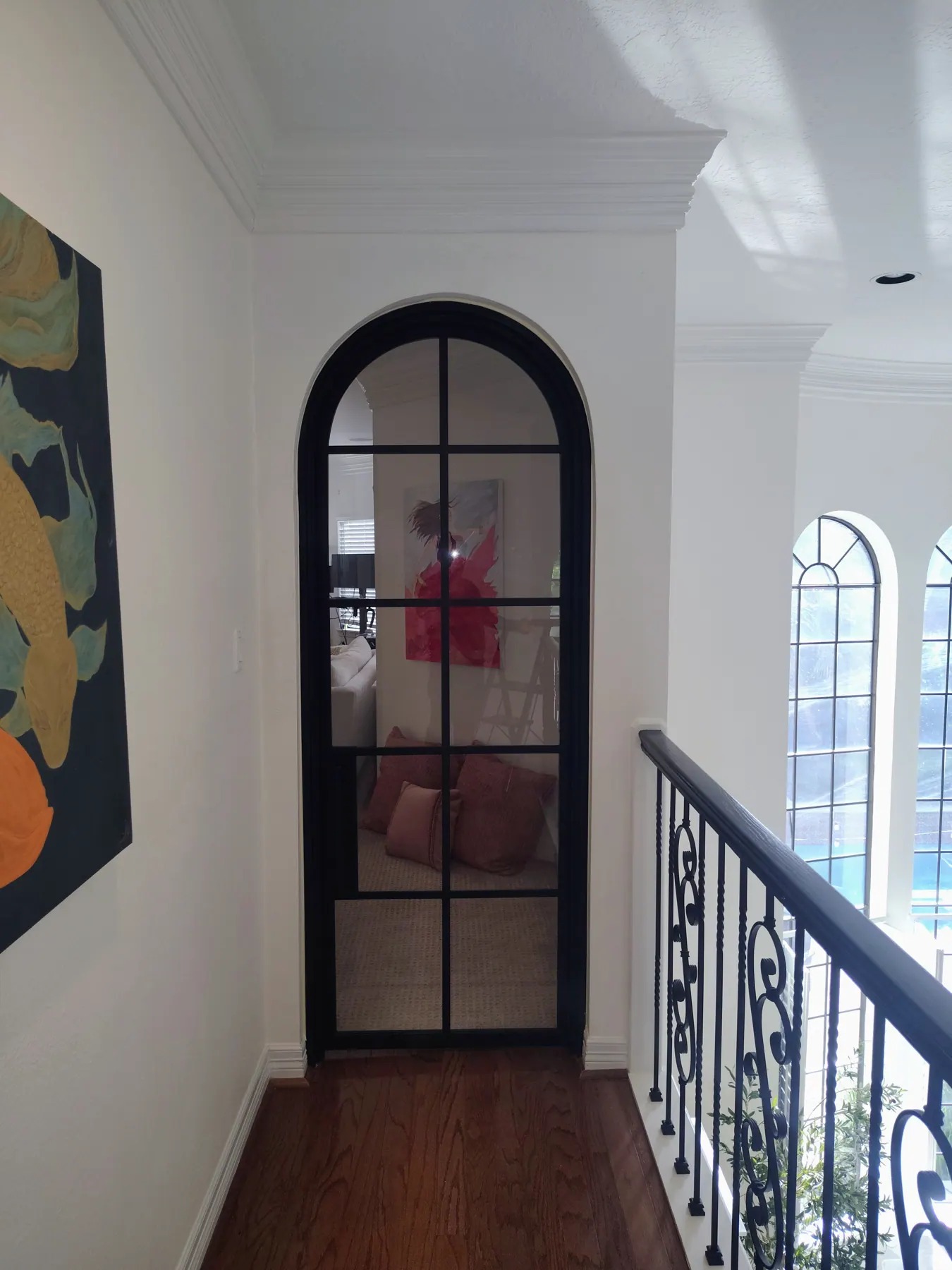 Black iron stair railing next to an arched iron door inside a home