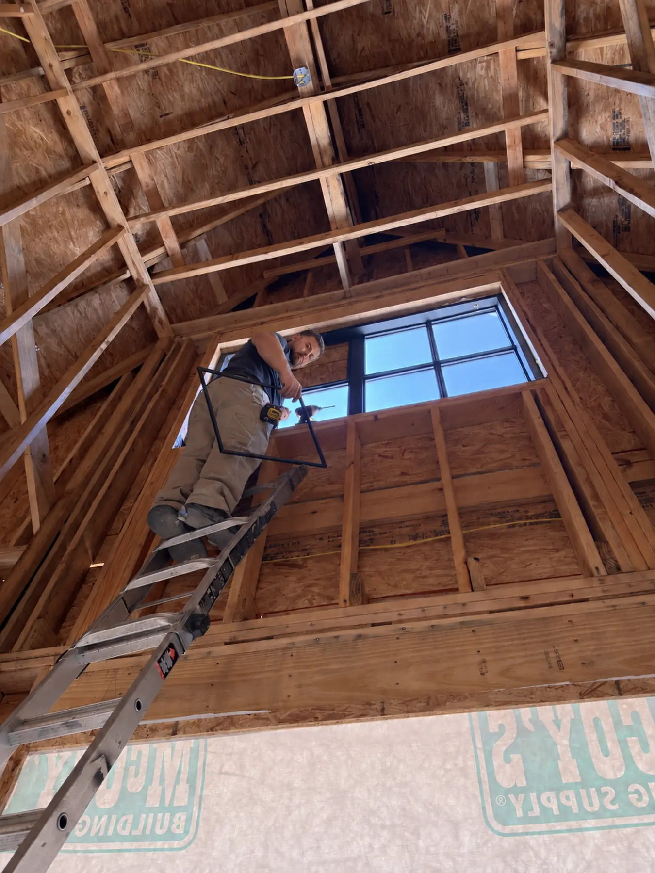 Installer setting a large window high in a vaulted room under construction